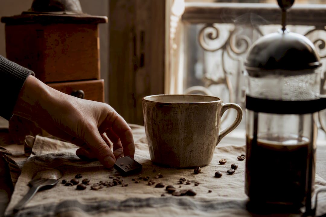 Hand placing chocolate near coffee cup in kitchen